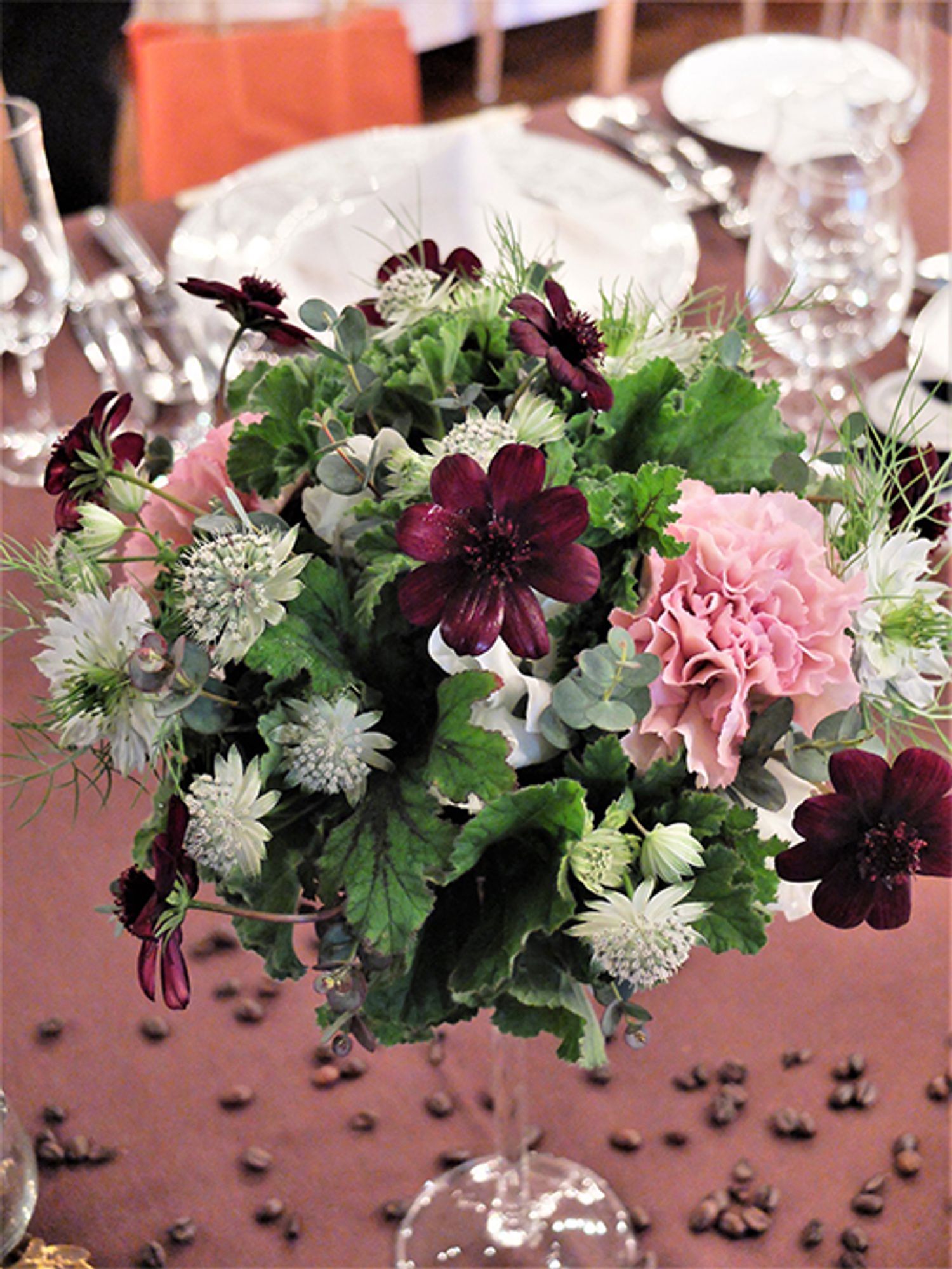 こちらは贈り花ではなく、ウエディングの会場を飾った花です。コーヒーを愛するお二人ということで、コーヒー色も連想させる褐色のチョコレートコスモスを使おうと考えました。さらにリーフもチョコレートゼラニウムを選びました。ニゲラ‘ミスジーキル’、スイートピー‘ロイヤルホワイト’、アストランティアなど白い小花の中にピンクベージュのカーネーション‘クレオラ’を加え、チョコレートコスモスを散らしました。コーヒー好きな二人というエピソードが招待されたお客様に伝わりますように……。