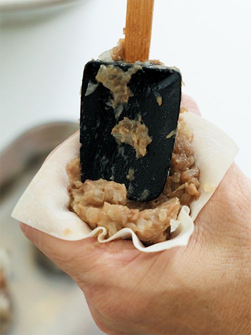 シューマイの皮にたねをのせ、親指と人さし指で輪を作って中にうめ込むようにして包む。少しくびれを作り、底面を平らにしたら完成。
