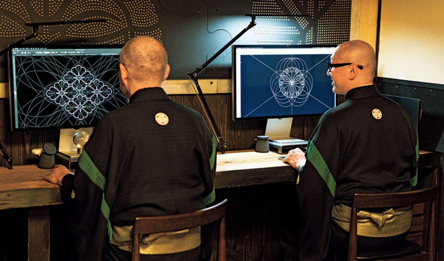 隣り合ってパソコンに向かう父・承龍さん（左）と、息子の耀鳳さん（右）。壁面を飾るのは、太鼓の鋲（びょう）で家紋を表現した工房の代表作「Mon×Studs」。ホテルや商業施設の内装にも採用された。