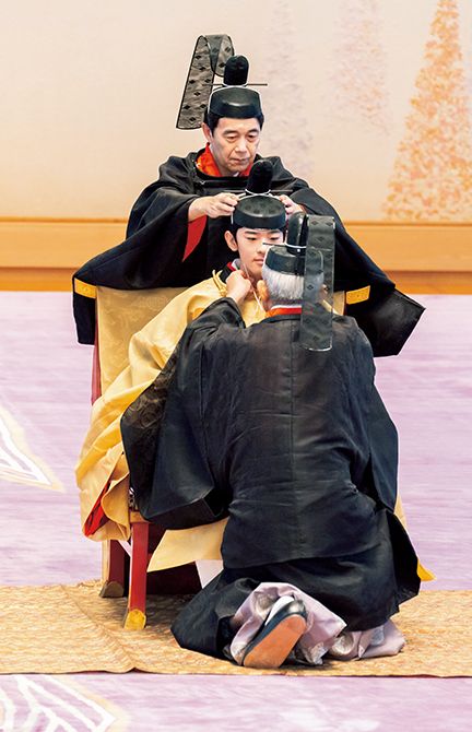 あごの下で掛緒を結んでいるのは加地隆治御用掛。後ろから冠を支えているのは小山永樹皇嗣職宮務官長。