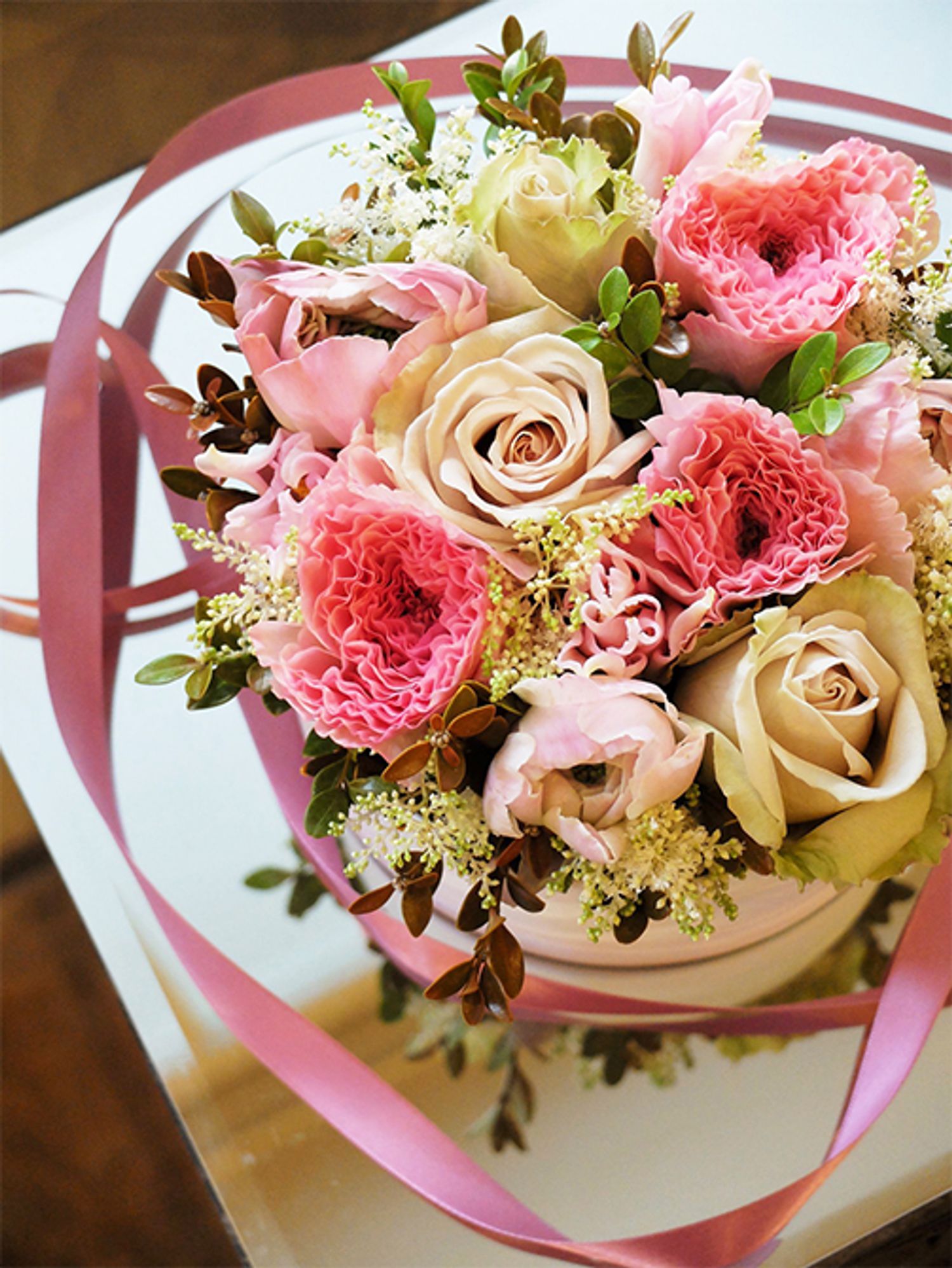 ピンク×淡いベージュの組み合わせを花箱にすると、どこかアンティークな雰囲気に。バラ、ラナンキュラス、チューリップ、と大きめの花を利用しましたが、すき間をアスチルベ‘ダイヤモンド’がきれいに埋めてくれます。バラは‘デザート’、ラナンキュラスは‘ちほの恋’、チューリップは‘ダイナスティーピクチャー’をセレクト。あしらいに紅ツゲを加えました。直径15cmのボックスを使用。
