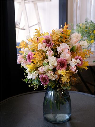 いつも明るく元気なお友達への誕生日祝いと聞いて、ピンクと黄色の花色合わせで、ブーケを制作しました。ピンクはスカビオサ‘シオリ’とスイートピー‘ドリーム’、チューリップ‘ドリーマー’。黄色はチューリップ‘イエロークラウン’と金葉アカシア‘ツトム’です。ピンクの同系色合わせは優しい印象ですが、黄色を加えたアレンジも明るい春らしくておすすめです