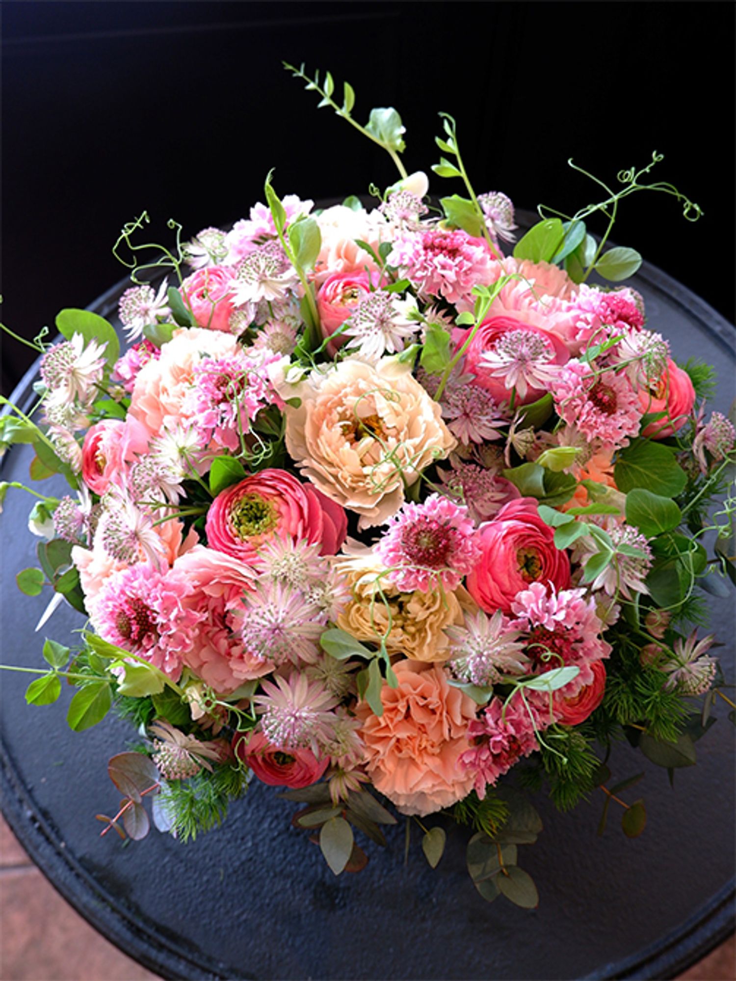 ご友人の息子さんへ、ご結婚のお祝いの贈り花のオーダーをいただき、この時期に出回る花を種類豊富に使い、華やかな雰囲気のアレンジを制作しました。スカビオサ‘シオリ’、ラナンキュラスの‘シャルロット クリーム’と‘ポー’、カーネーション‘シルクミナミ’、アストランティアなどを使用。エンドウマメのつるで動きをつけています。