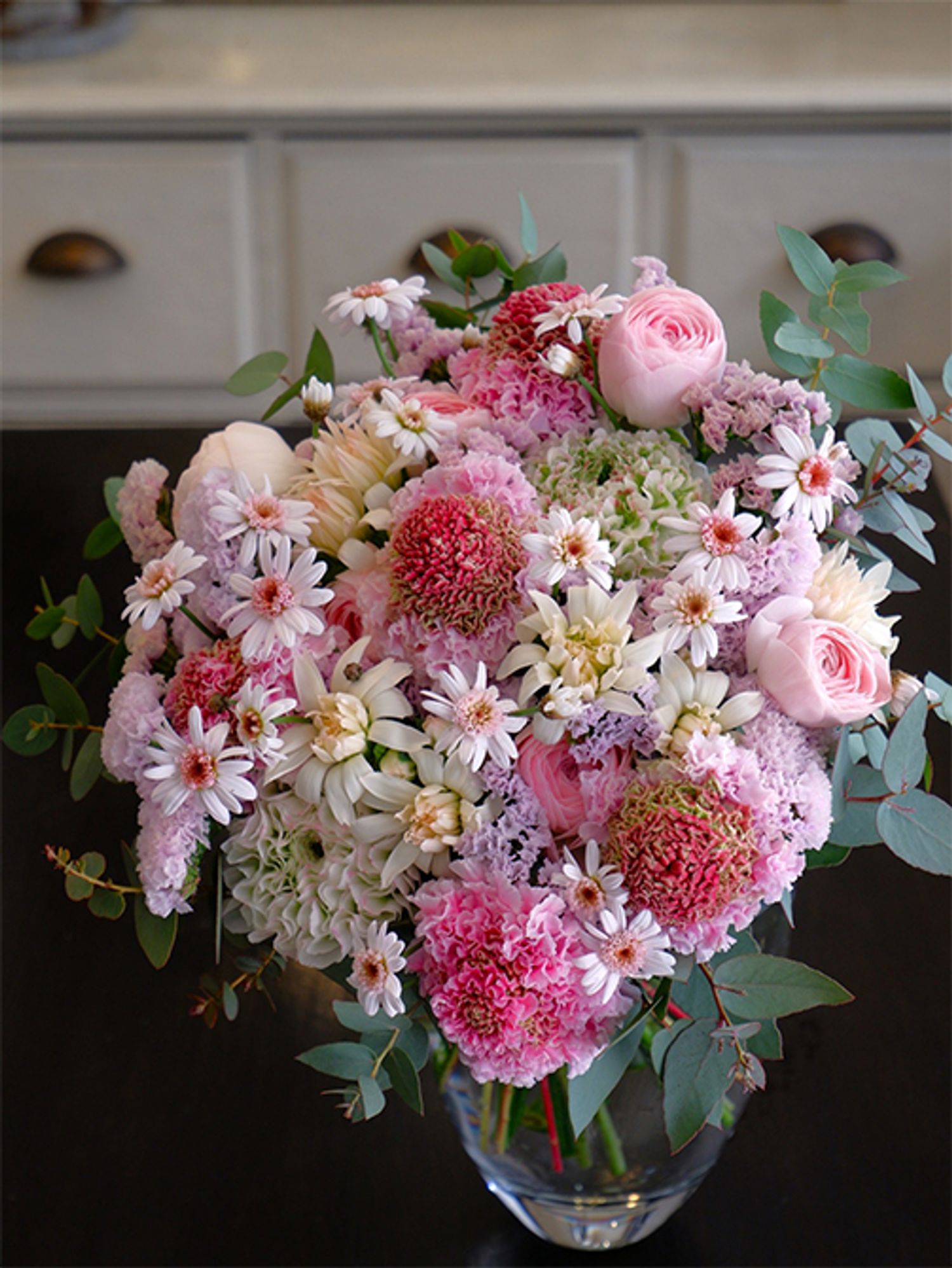 新しく社会人になる姪御さんにお祝いの贈り花。寺尾さんオリジナルのスカビオサ‘ハルル’をメインに、マーガレット‘ドリームカシス’、カーネーション‘ミニティアラ ミルク’、スターチス‘ソロモン’、ラナンキュラスの‘ポンポン キャスパー’と‘エアリアル’など、春のピンクブーケに。シルバーリーフのユーカリでナチュラル感をプラス。