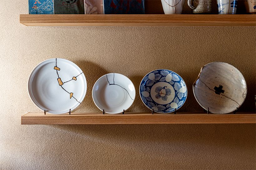 大工原さんの作品。左から、竹の鎹（かすがい）と黒漆で継いだ現代もののプレート、黒漆で継いだ現代作家の小皿、茄子の模様に合わせてヒビを直した染付皿、ヒビに漆を染み込ませ、欠けの断面には銀を蒔いた現代作家のプレート。