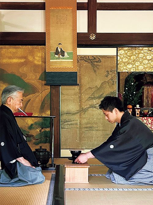 小堀宗実家元が点てたお茶を取り上げる若宗匠。家元は捧げるお茶に息がかからないよう、白い和紙の「へだて」を使用している。