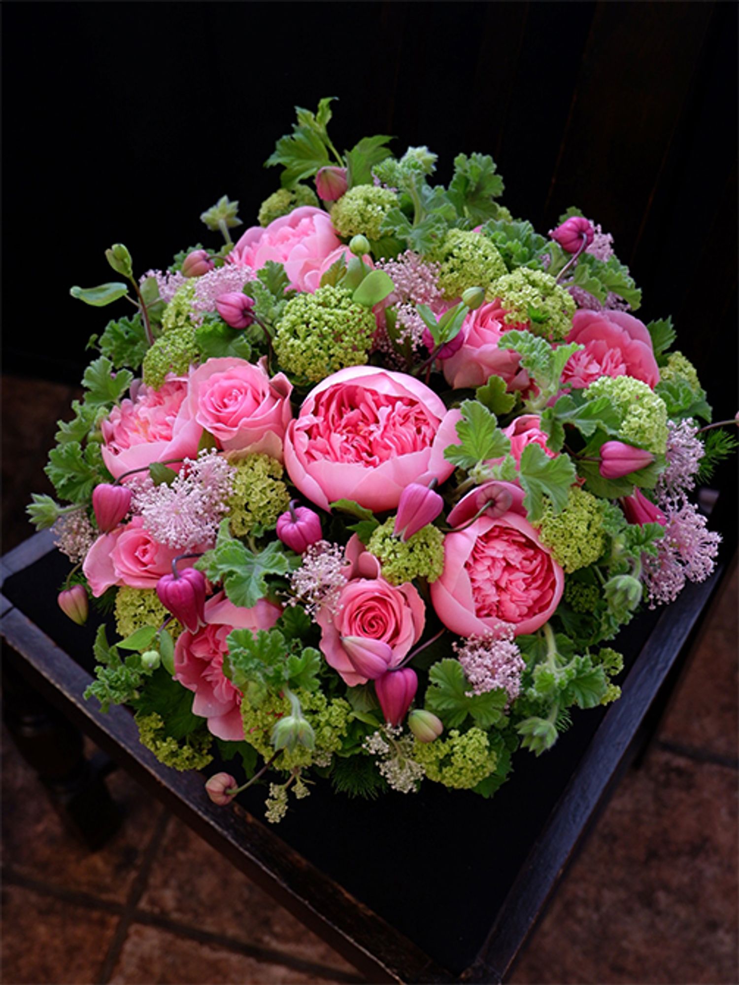 ご両親から娘さんへ、結婚祝いの贈り花を。ピンクとフレッシュグリーンの花色合わせで、かわいらしいながらもパッと目立つアレンジを制作しました。この時期に出回るシャクヤクのボリューム感と、セアノサス‘マリーサイモン’の繊細さ。これはとても相性のよい組み合わせだと感じます。シャクヤクは‘エッチドサーモン’を使用。ほかにバラ‘ブロッサムピンク’、クレマチス‘天使の首飾り’を合わせ、濃淡ピンクの花色合わせにしました。みずみずしい緑色は、ビターチョコゼラニウムとビバーナム・スノーボールです。