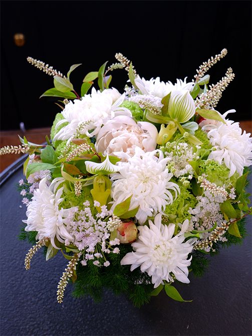 ヒメリョウブは白といっても少しクリームがかった花色なのですが、マムの白花と合わせると、そのニュアンスの違いがよくわかります。明るさのある純白の花の中で、周囲に散らしたヒメリョウブは引き締め役にもなっています。マムは‘セイ マノアホワイト’を使用。ほかに、シャクヤク‘ホワイトピーチ’、リシアンサス‘アンバーダブルモヒート’、パフィオペディルム、ブルーレースフラワー‘ピュアレディ’を選びました。