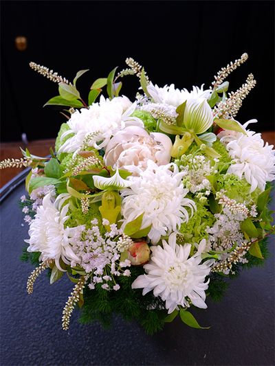 ヒメリョウブは白といっても少しクリームがかった花色なのですが、マムの白花と合わせると、そのニュアンスの違いがよくわかります。明るさのある純白の花の中で、周囲に散らしたヒメリョウブは引き締め役にもなっています。マムは‘セイ マノアホワイト’を使用。ほかに、シャクヤク‘ホワイトピーチ’、リシアンサス‘アンバーダブルモヒート’、パフィオペディルム、ブルーレースフラワー‘ピュアレディ’を選びました。