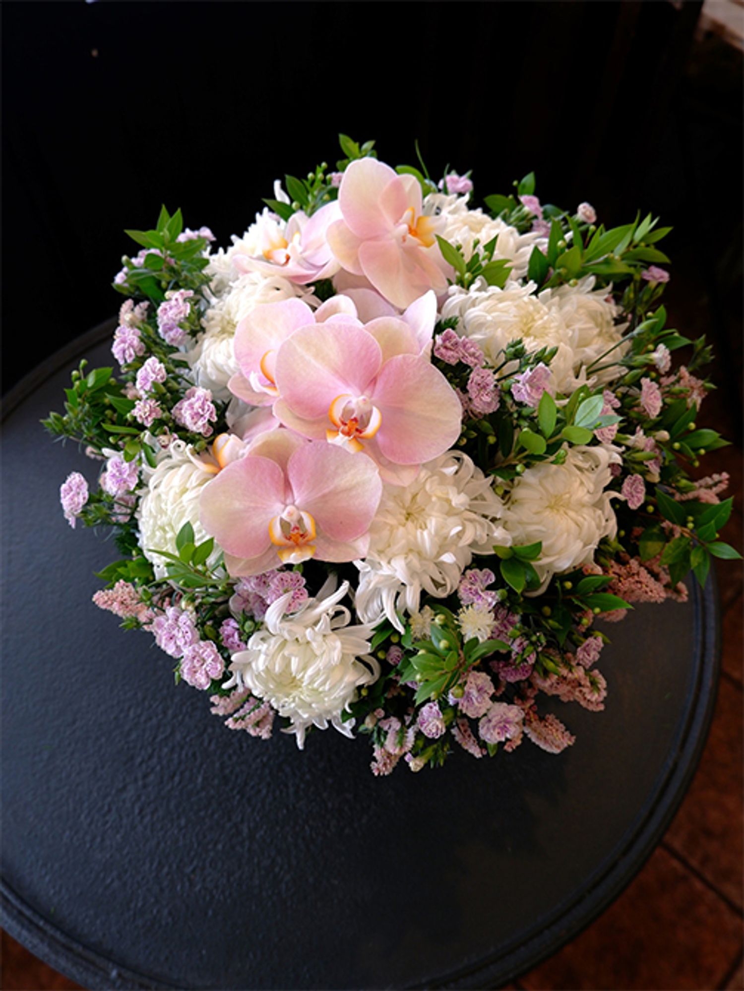 ダイアンサス‘ラフィーネ ピア’とファレノプシス‘ゼウスピンクベージュ’。似た花色ながら、花サイズが極端に異なる2種を対比させたアレンジです。白花のマム‘セイ マノアホワイト’でボリュームアップし、宿根スターチス‘キャラメル’も加えました。全体に散らばるように挿した‘ラフィーネ ピア’でアレンジがより華やかな印象に。