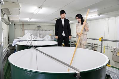 醪室で酒造りについて説明を受ける高瀬さん。本格的な酒造りが始まる秋・冬に備え、タンク内は空っぽに。酒をかき混ぜる櫂棒を手にして「こんなに重いもの久しぶりに持ちました」と驚いた様子。