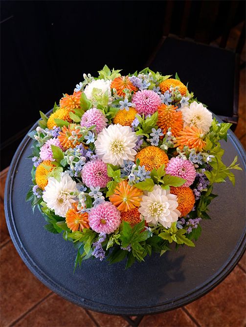 トリトマ‘ローペリ’とダリア、マムの花合わせでもう1点ご紹介。こちらはお誕生日を祝う贈り花です。ダリアは‘ウィムジー’と‘ベイピンク’、マムは‘パラドフダーク’。オキシペタルム‘ピュアブルー’やスターチス‘アイスブルー’などの青花を加え、パステルカラーの優しいミックスのアレンジに。フレッシュグリーンの葉はテマリシモツケのルテウスです。