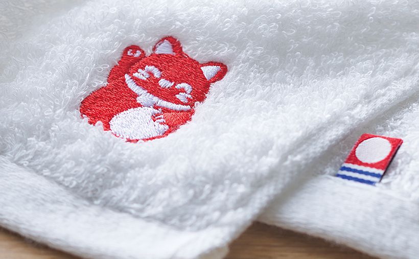 ご購入特典のオリジナルフェイスタオルは34×80cm、綿100％の今治製。招き猫の刺繡を施しました。