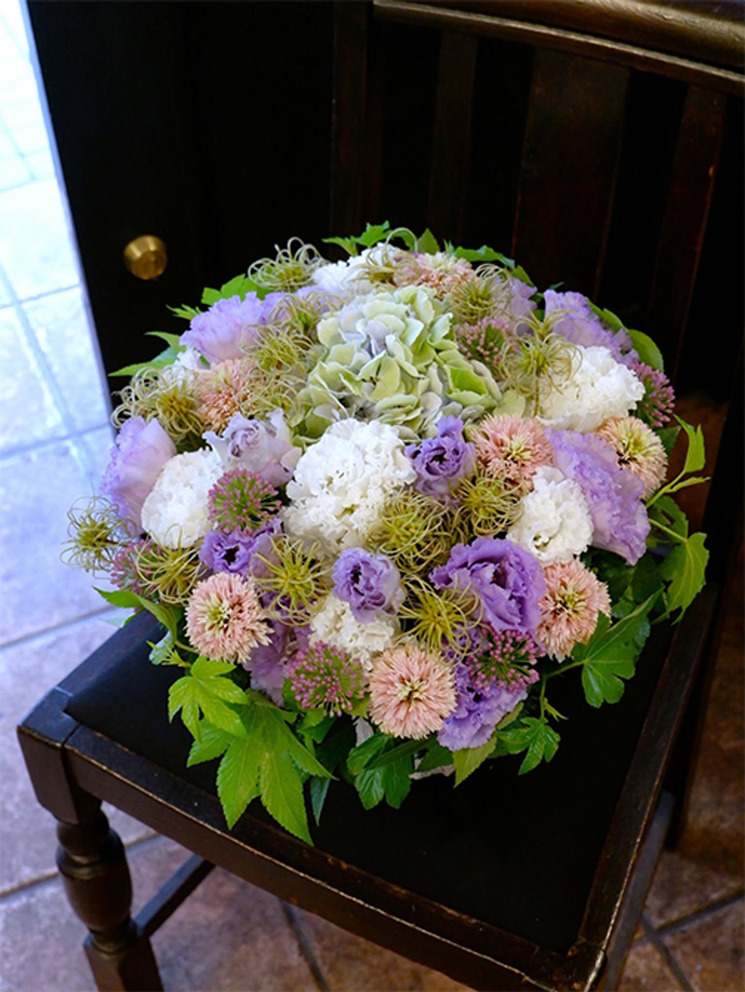 クレマチスは初夏の花後にタネをつけます。くるくる巻きの形状がユニークで、切り花でも人気となっています。そのクレマチスシードをアクセントにしたアレンジがこちら。リシアンサスの‘ボヤージュスノー’と‘NFラベンダー’、アジサイ‘ベレナアンティークブルー’、エキナセア‘チェリーフラッツ’、アリウム‘サマービューティー’、キイチゴ‘ベビーハンズ’などを利用。花と花のすき間を埋めるようにクレマチスシードを加えると、優しいパステルカラーでありながら、大人っぽい雰囲気に仕上がります。