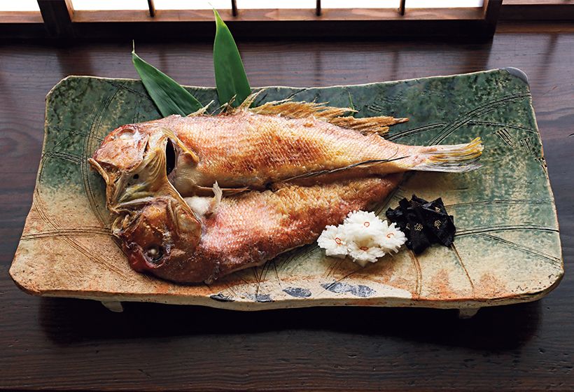 魯山人がうろこごと食べるところに風情とおいしさがあると説いた若狭ぐじ姿焼を、幅約50センチの織部秋草文俎板鉢に盛って。“食器は料理のきもの”として器と料理の関係を重要視していた魯山人が考案したとされるまな板皿は、力強い造形で圧倒的な存在感を放つ。